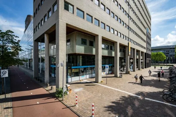 Gebouw aan het Johanna Westerdijkplein met winkels onderin en voetgangers op het plein ernaast.